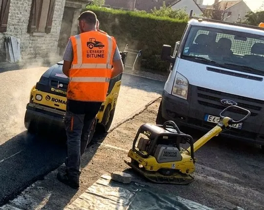 Ouvrier en gilet L'Expert Bitume près d'un rouleau compresseur et d'une plaque vibrante